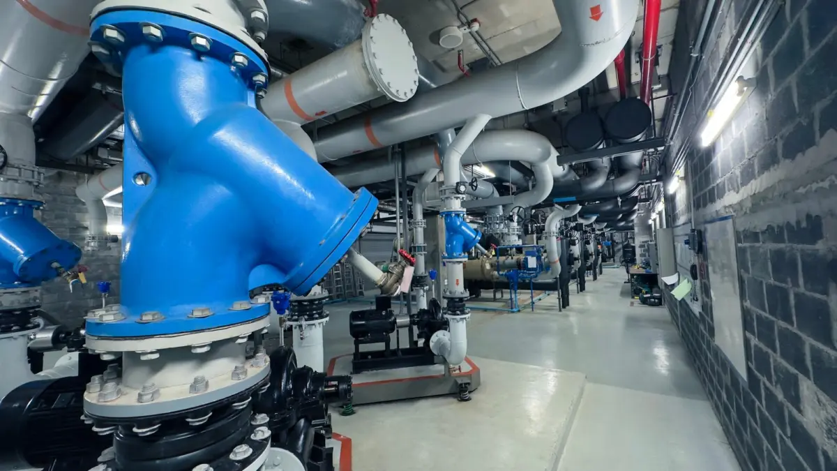 Gang in einem Technikraum mit gedämmten Rohrleitungen und blauen Armaturen