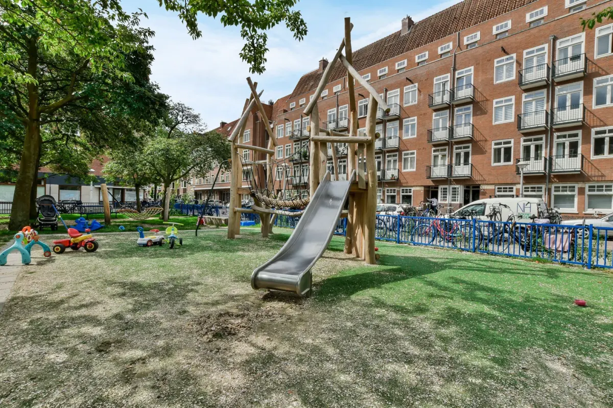 Spielplatz mit Holzgerüst und Rutsche vor einem Backstein-Wohnblock