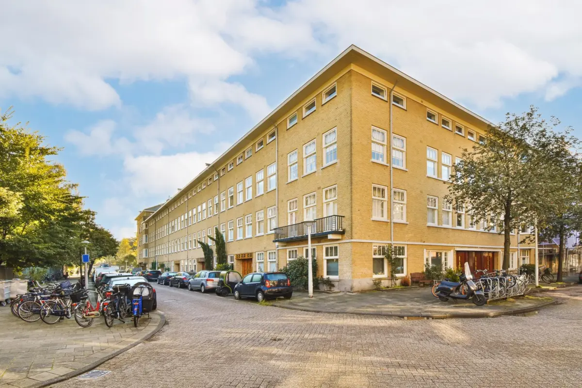 Langgestrecktes gelbes Klinkergebäude an einer Straße, davor Fahrräder und Autos